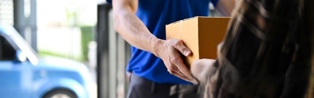 Close up view of delivery man in blue uniforms handing the parcel  to customer while standing in front of his van
